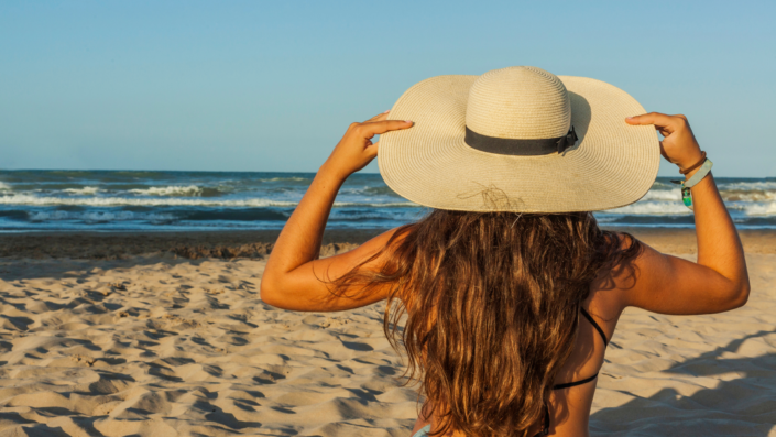 A young woman wearing a big, floopy hat at the beach